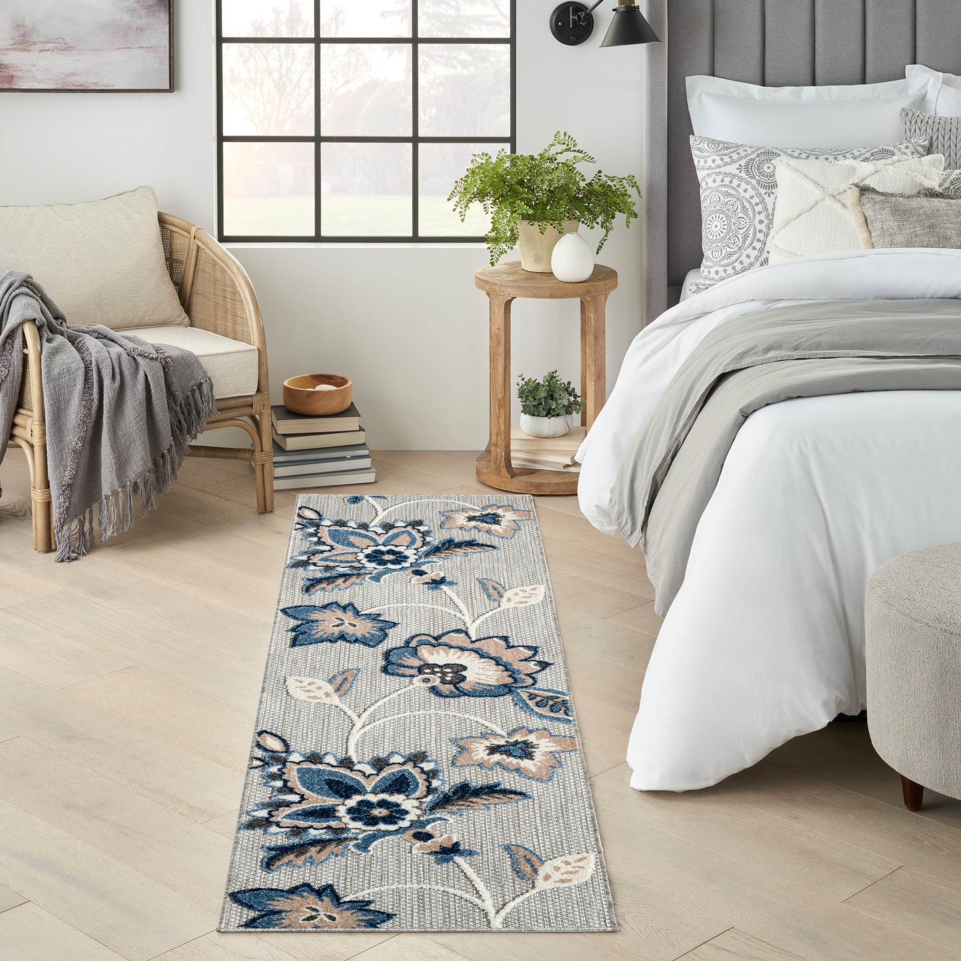 Blue floral patterned runner rug on light wood floor beside a white bed with gray bedding and wicker chair.