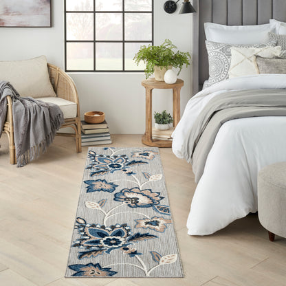 Blue floral patterned runner rug on light wood floor beside a white bed with gray bedding and wicker chair.