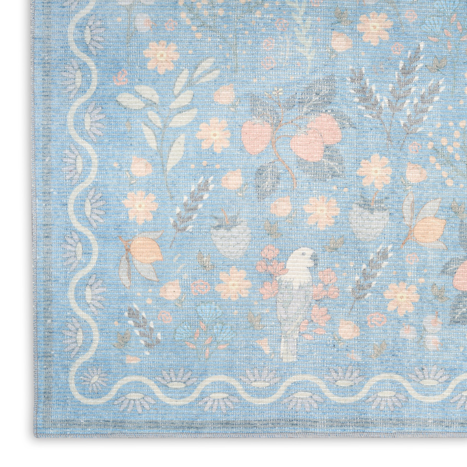 Pastel blue woven rug featuring pink and cream florals and a white scalloped border with a small bird motif.