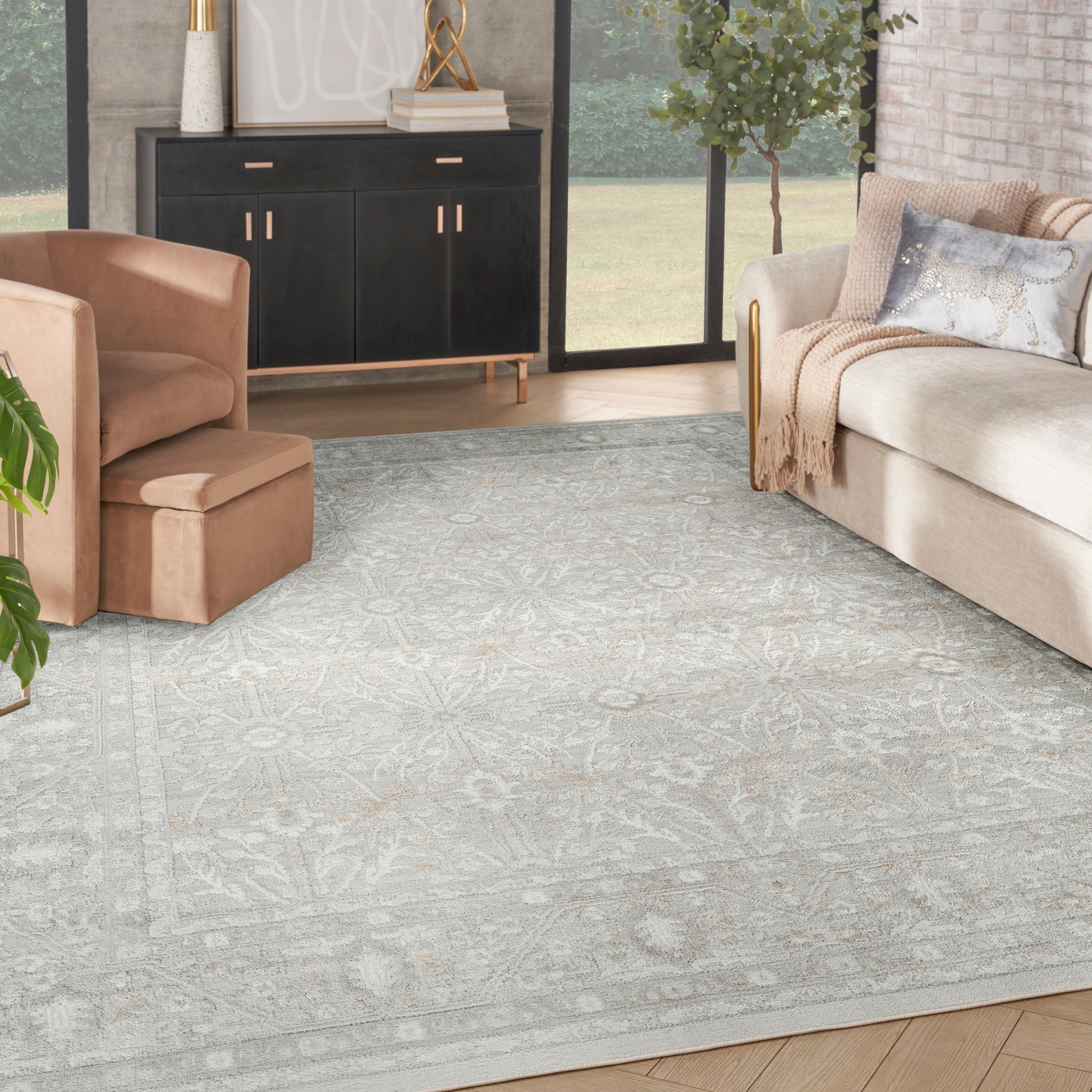 Light gray patterned area rug on wood floor in a modern beige living room with tan chair, beige sofa, and black cabinet.