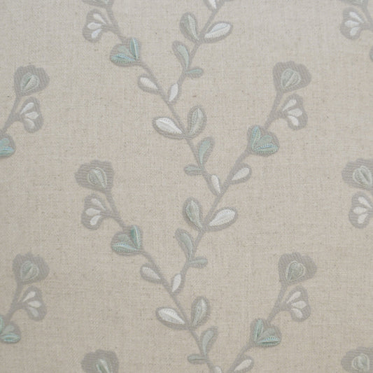 Beige linen fabric with delicate pale blue-green embroidered vine pattern and small leaves.