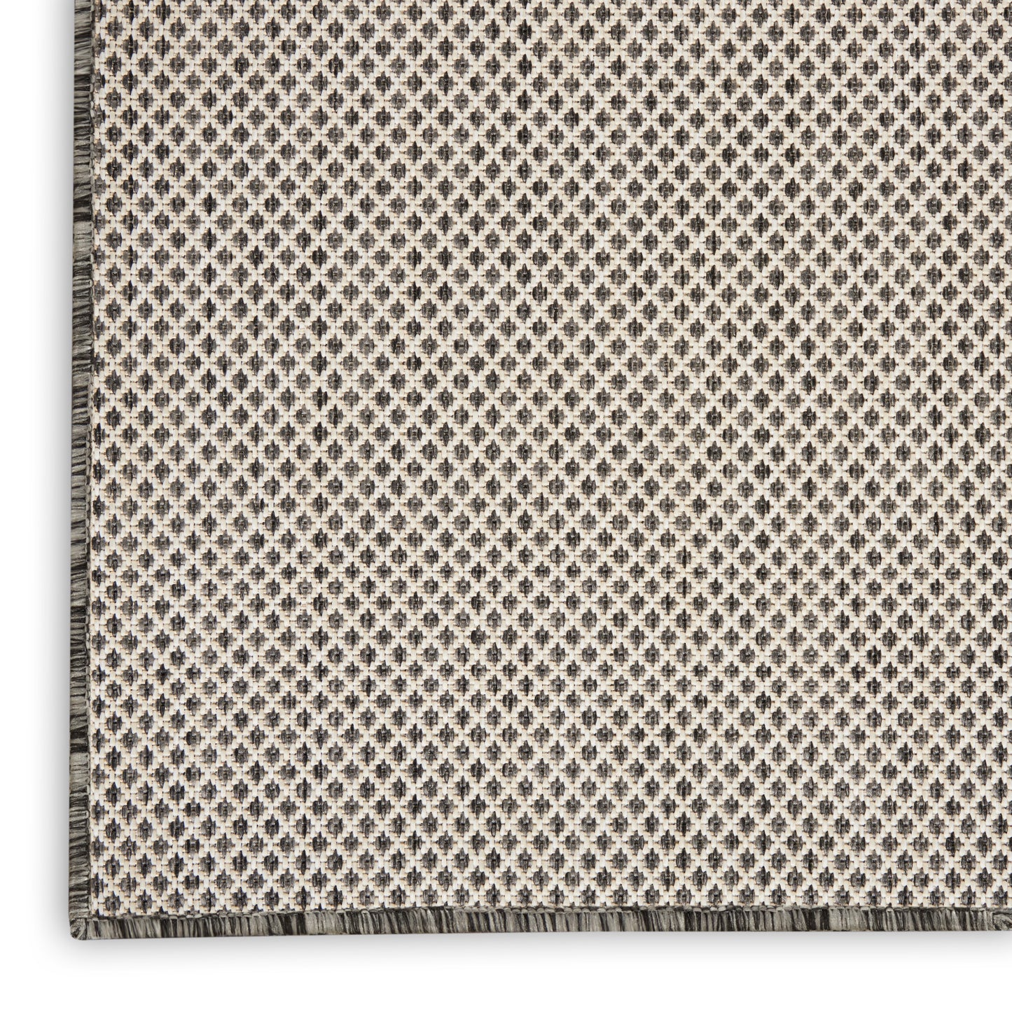 Close-up of a beige woven area rug with a tiny gray diamond pattern and fringe along the edge.