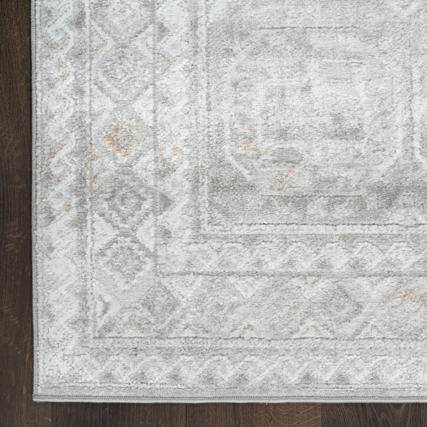 Distressed light gray area rug with geometric border and ivory beige accents on dark wooden floor.
