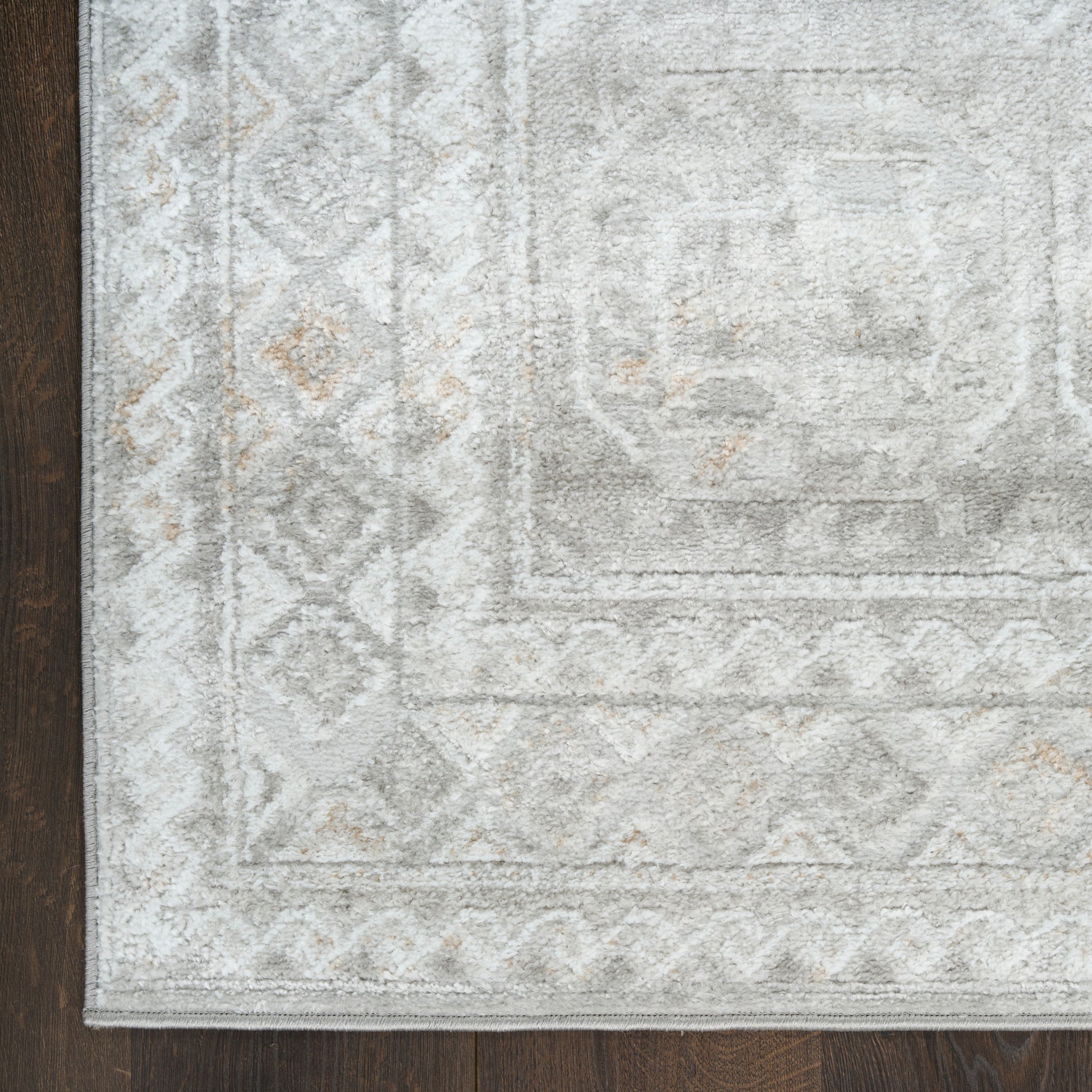 Distressed light gray area rug with geometric border and ivory beige accents on dark wooden floor.