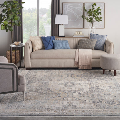 Beige fabric sofa with blue and gray textured cushions, a throw blanket, abstract wall art, plants, and a patterned rug.