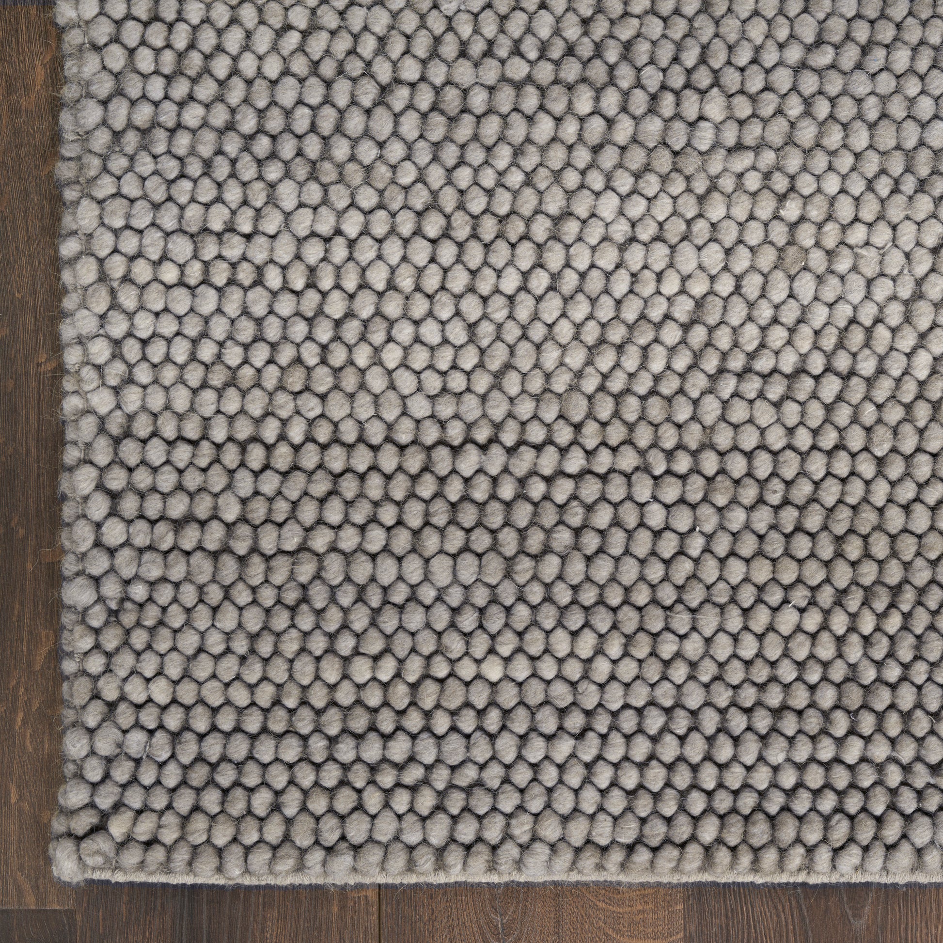 Gray looped-pile area rug with dense rounded tufted texture on dark wood floor.