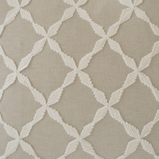 Beige fabric with white raised embroidery forming a diamond lattice pattern of leaf-shaped motifs.