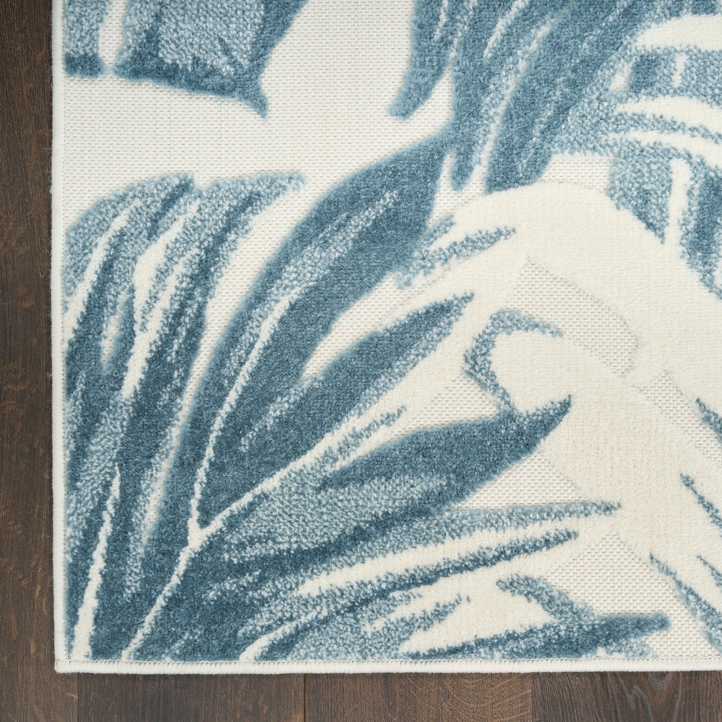 Blue palm-leaf patterned rug with cream background; textured pile, bound edge, rectangular living-room decor.