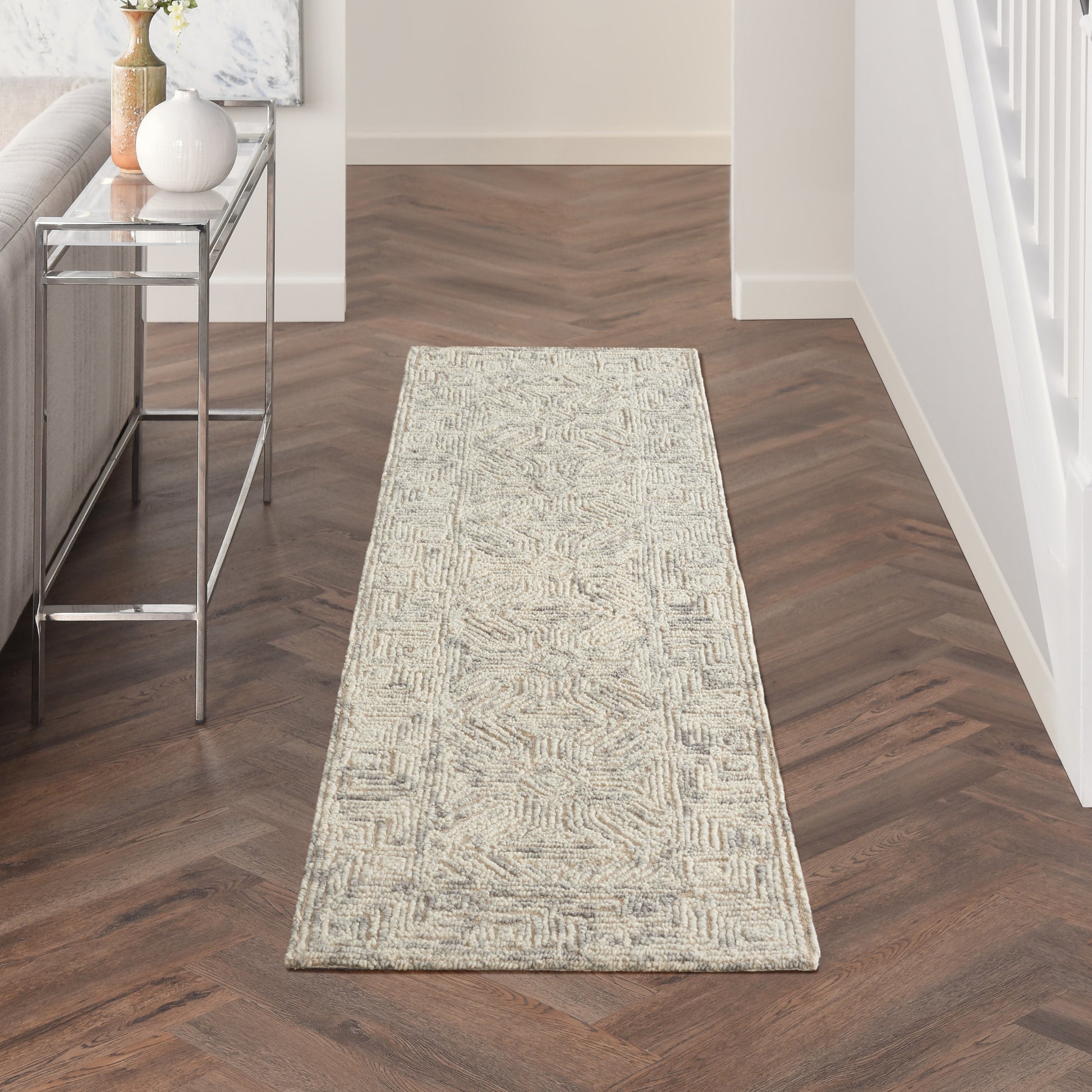 Beige geometric runner rug on dark herringbone floor beside a metal console table with vases.