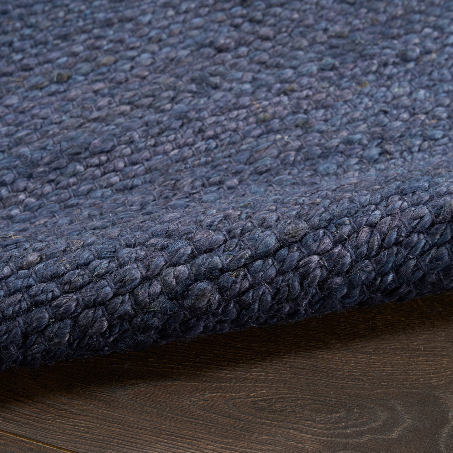 Dark navy boucle rug with dense chunky loop pile, folded edge on wooden floor.