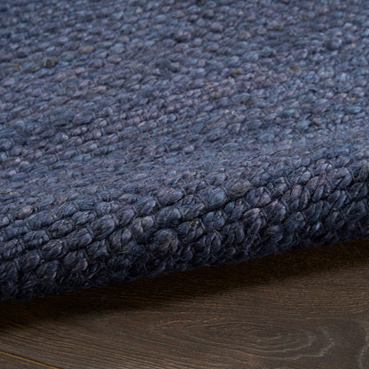 Dark navy boucle rug with dense chunky loop pile, folded edge on wooden floor.