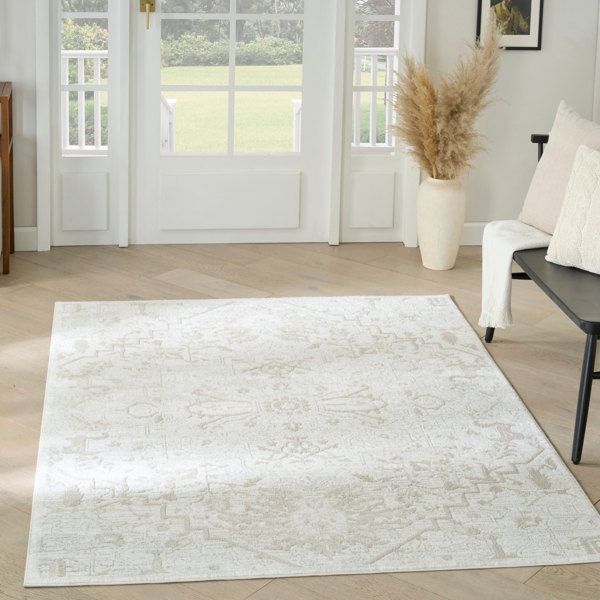Cream-toned area rug with a subtle geometric pattern on light wood flooring in a bright living room, pampas vase nearby.