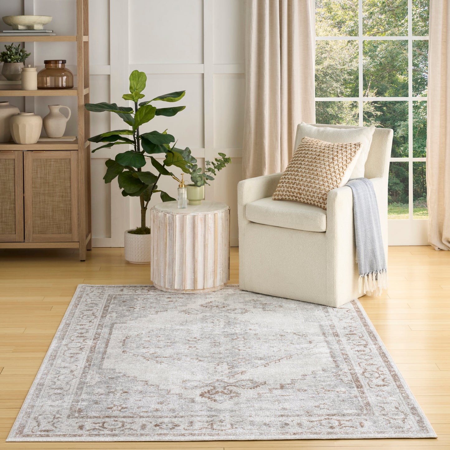 Neutral-toned area rug with a subtle faded border, cream armchair and round wood side table in a cozy living room.