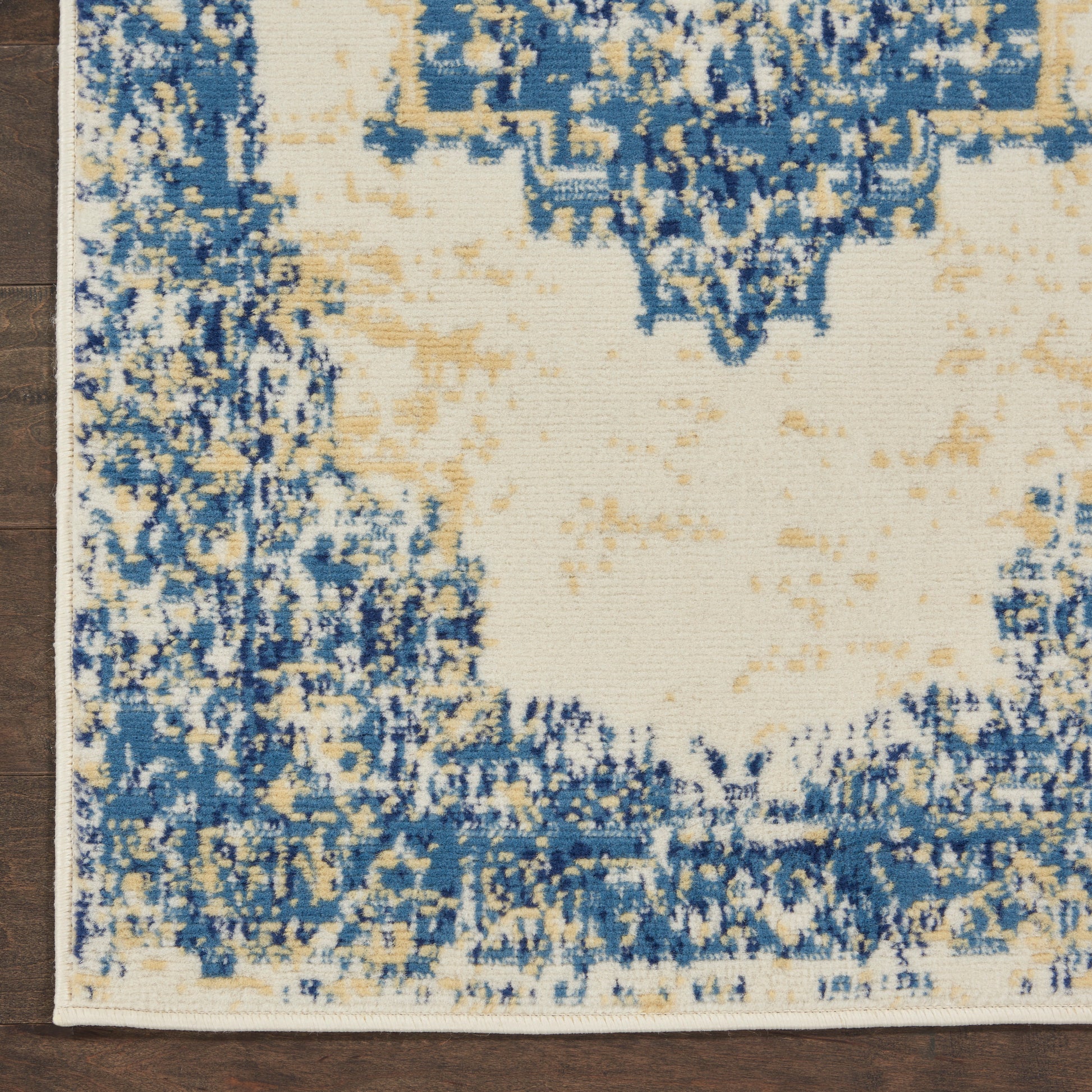 Distressed abstract blue & cream rug with beige accents, cream center and blue border on wood floor.