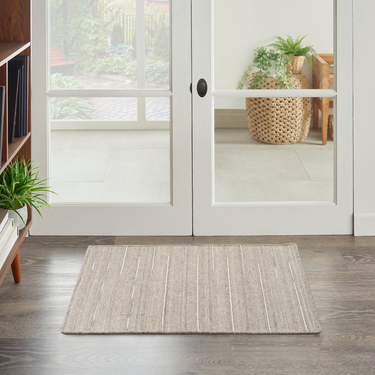 Beige flatweave rug with subtle white and pale blue stripes on dark wood floor in front of white-framed glass French doors.