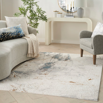 Neutral living room with a curved light-gray sofa, blue patterned cushion, beige throw, gray armchair, plant, and abstract rug.