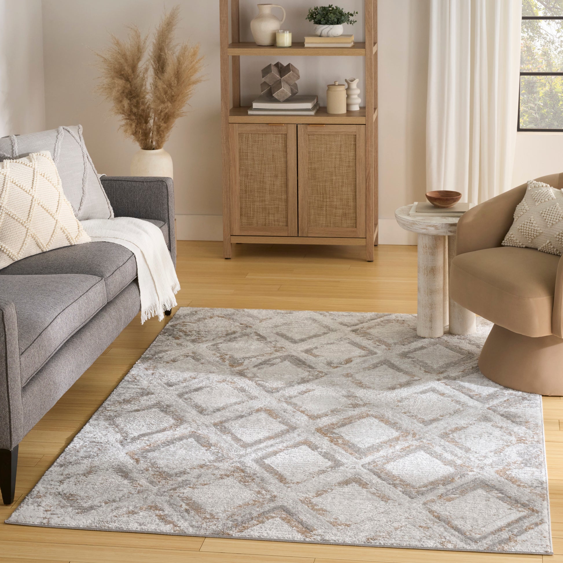 Neutral living room with light gray geometric rug, gray sofa, beige accent chair, woven cabinet, and pampas grass decor.