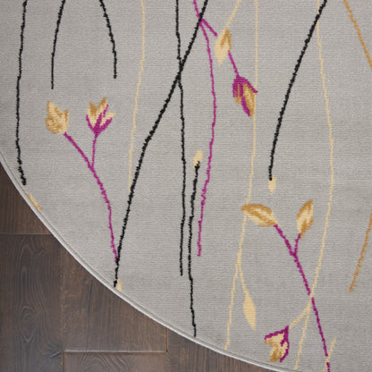 Round light gray rug with black, magenta and yellow abstract botanical lines on dark wood floor.