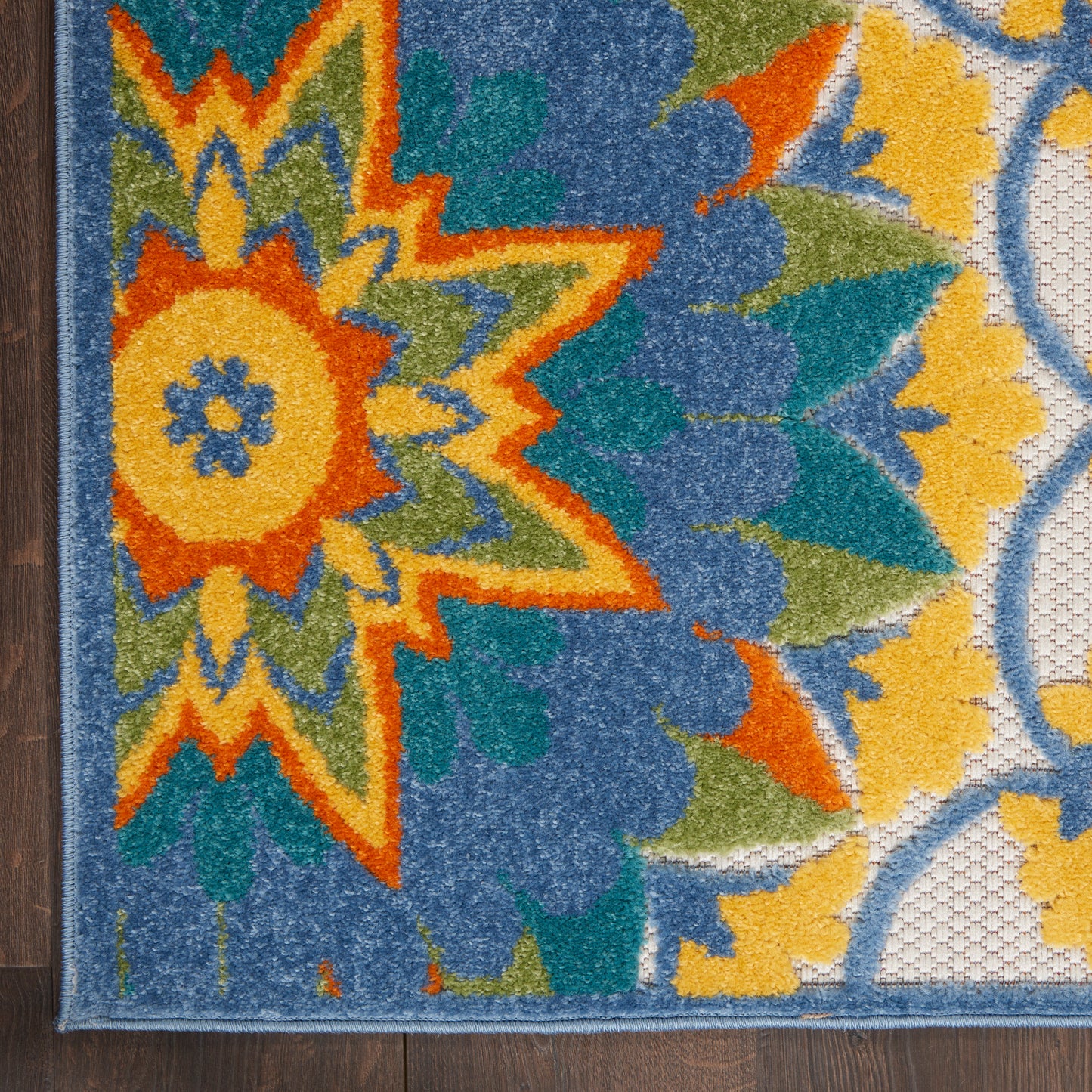 Close-up of a vibrant boho area rug with a large orange-yellow flower, teal and blue petals, green accents, and a dark border.