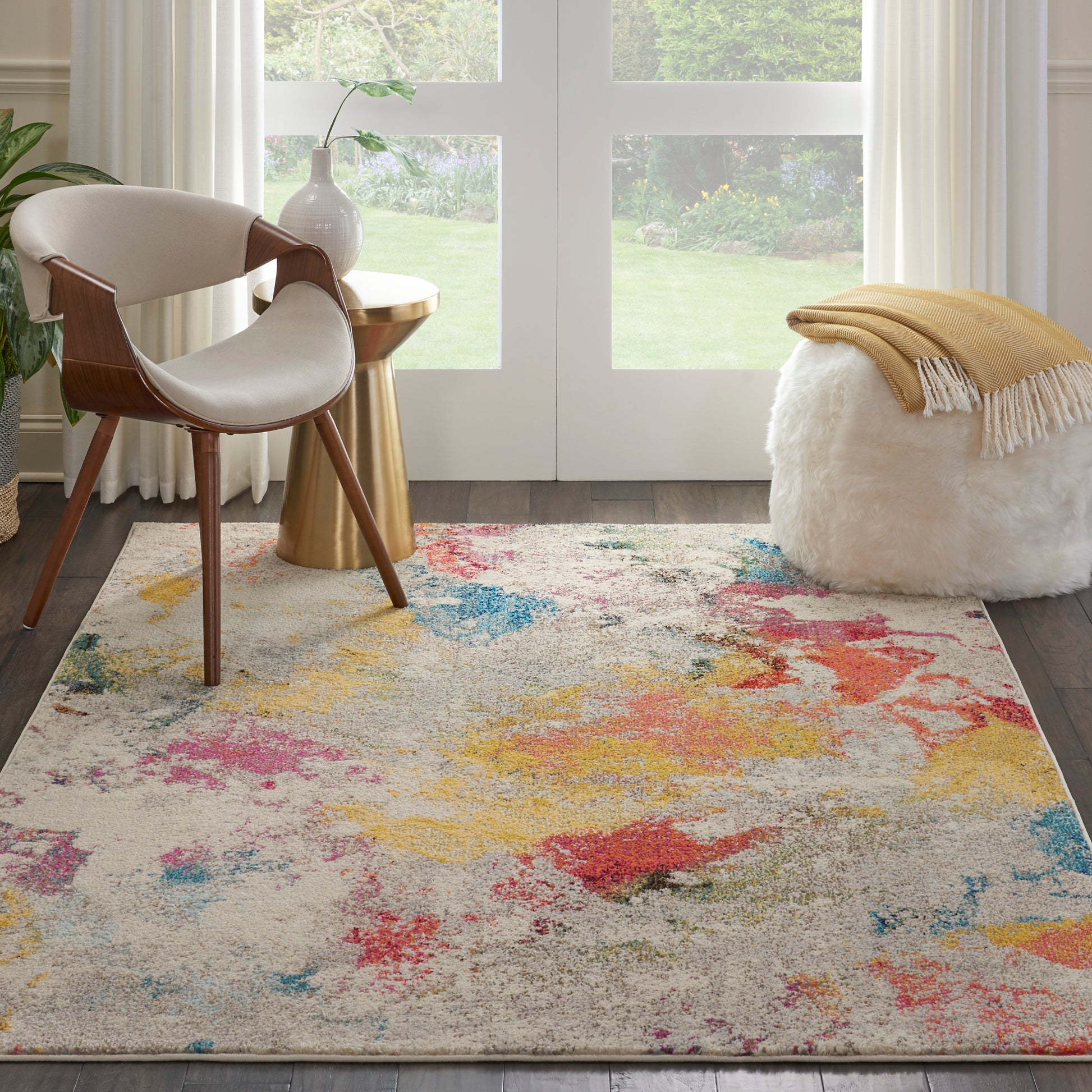 Contemporary living room with a multicolor abstract rug, mid-century wood chair, gold table, white pouf and mustard throw.
