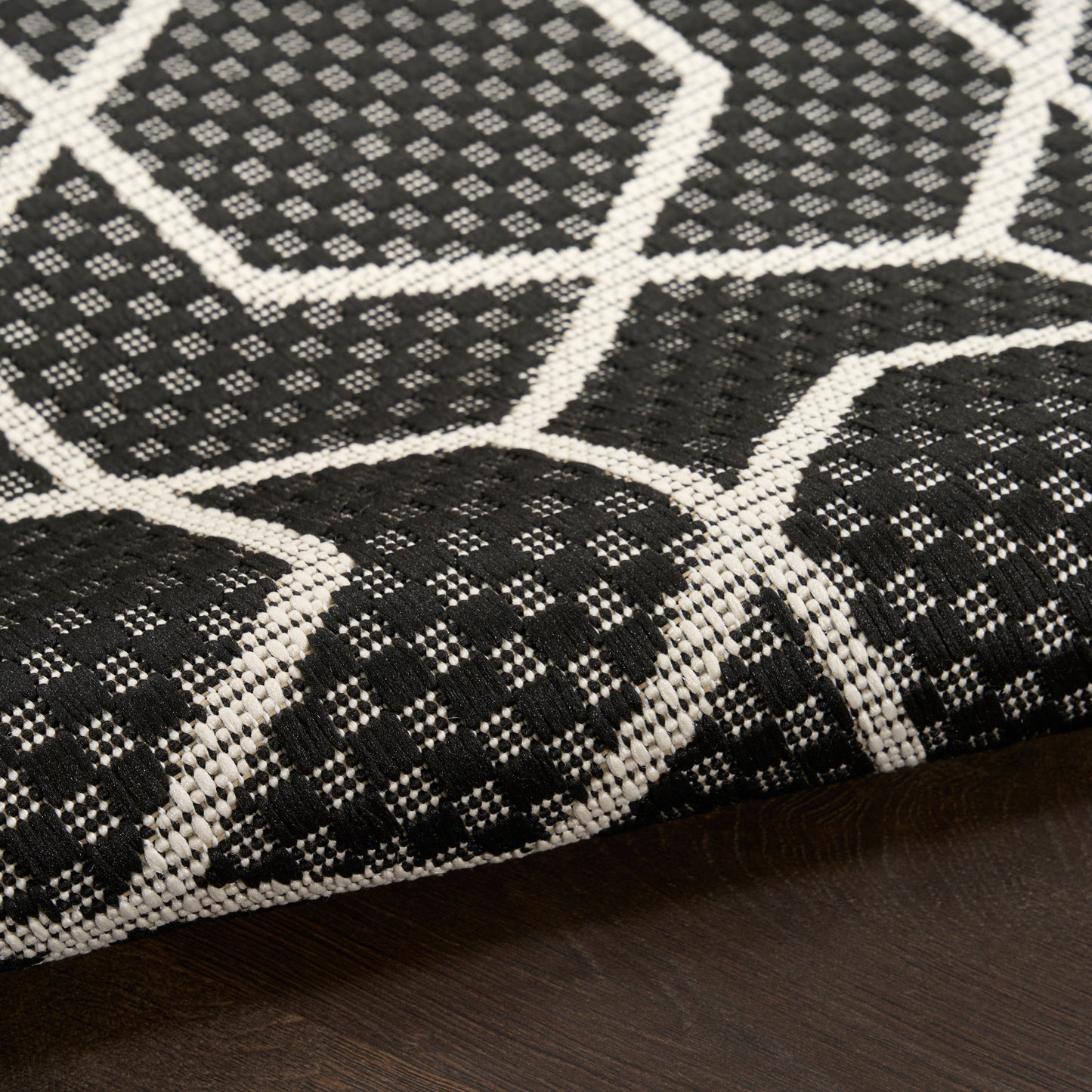 Black and white woven rug with bold hexagonal lattice pattern, geometric style on a wooden floor.