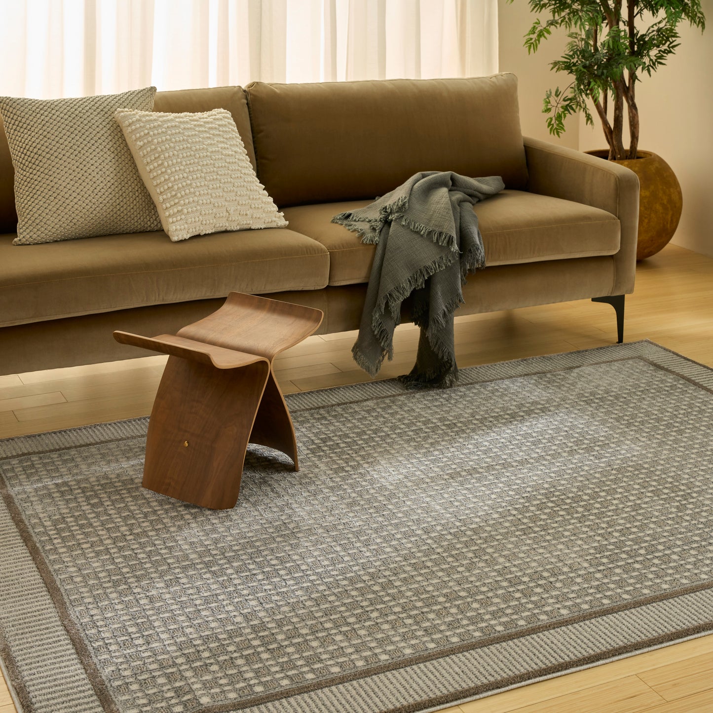 Brown sofa with textured cushions, gray throw, sculptural wooden side table, and gray patterned area rug.