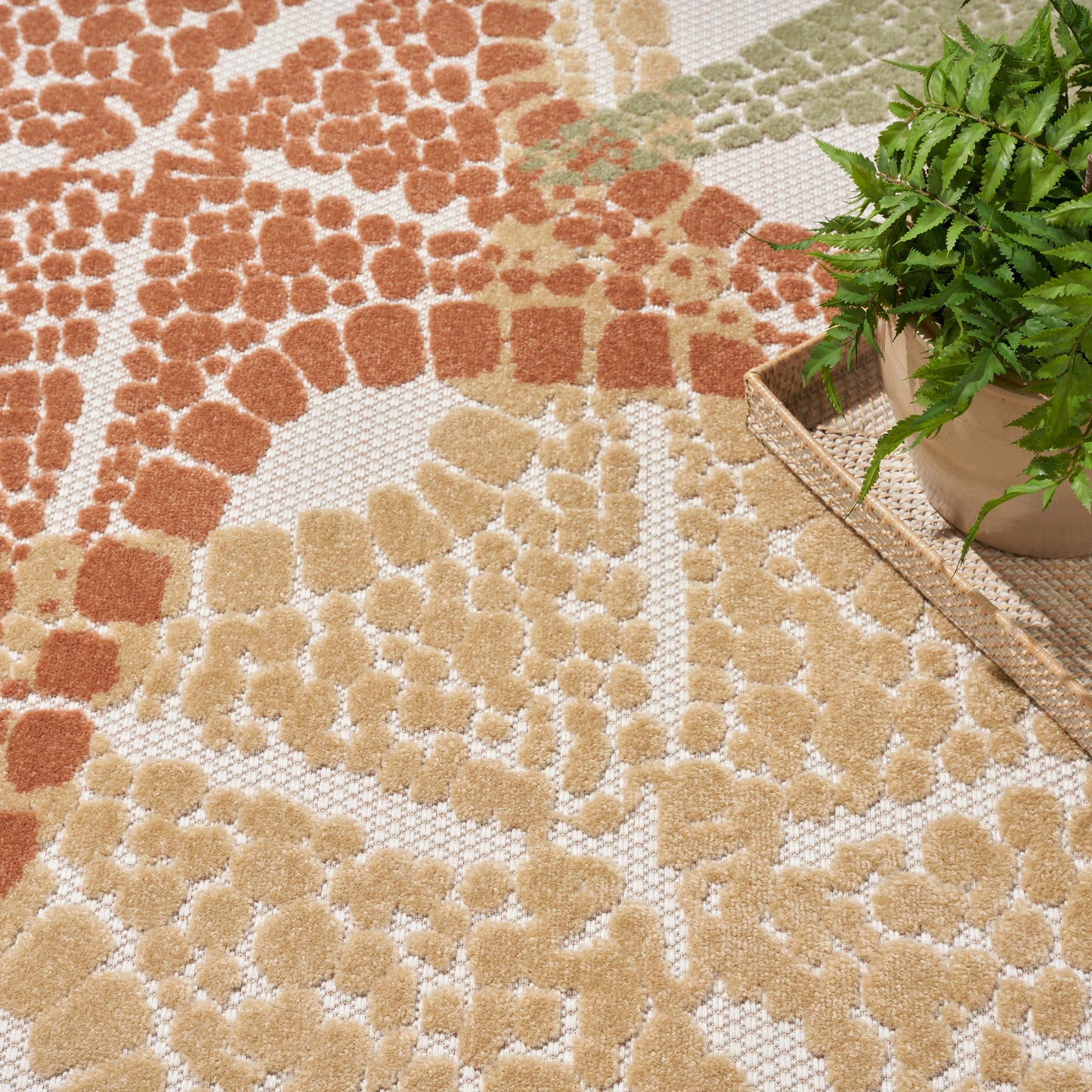 Warm-toned textured area rug with abstract floral pattern in terracotta, tan & beige; plush boucle pile beside potted plant.
