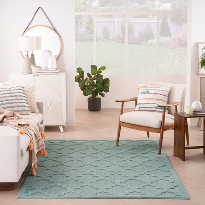 Teal geometric area rug in a modern Scandinavian living room with a white sofa, wooden armchair, cushions, and plant.