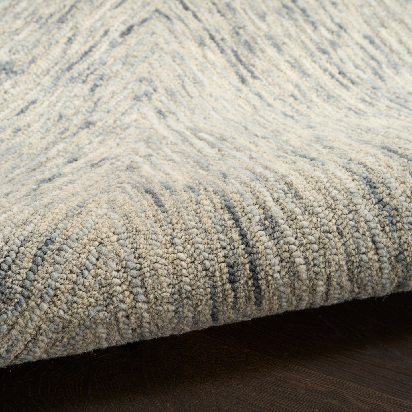 Close-up of a grey-blue loop-pile rug with a subtle, wavy stripe pattern on dark wood floor.