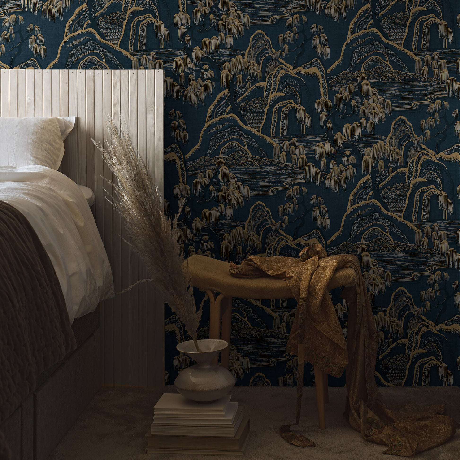 Bor?�stapeter Indigo Garden 3132 wallpaper featuring a stylized oriental garden in indigo and gold, with willow trees and scenic hills. Displayed on a feature wall, ideal for elegant interior design in bedrooms or living spaces.