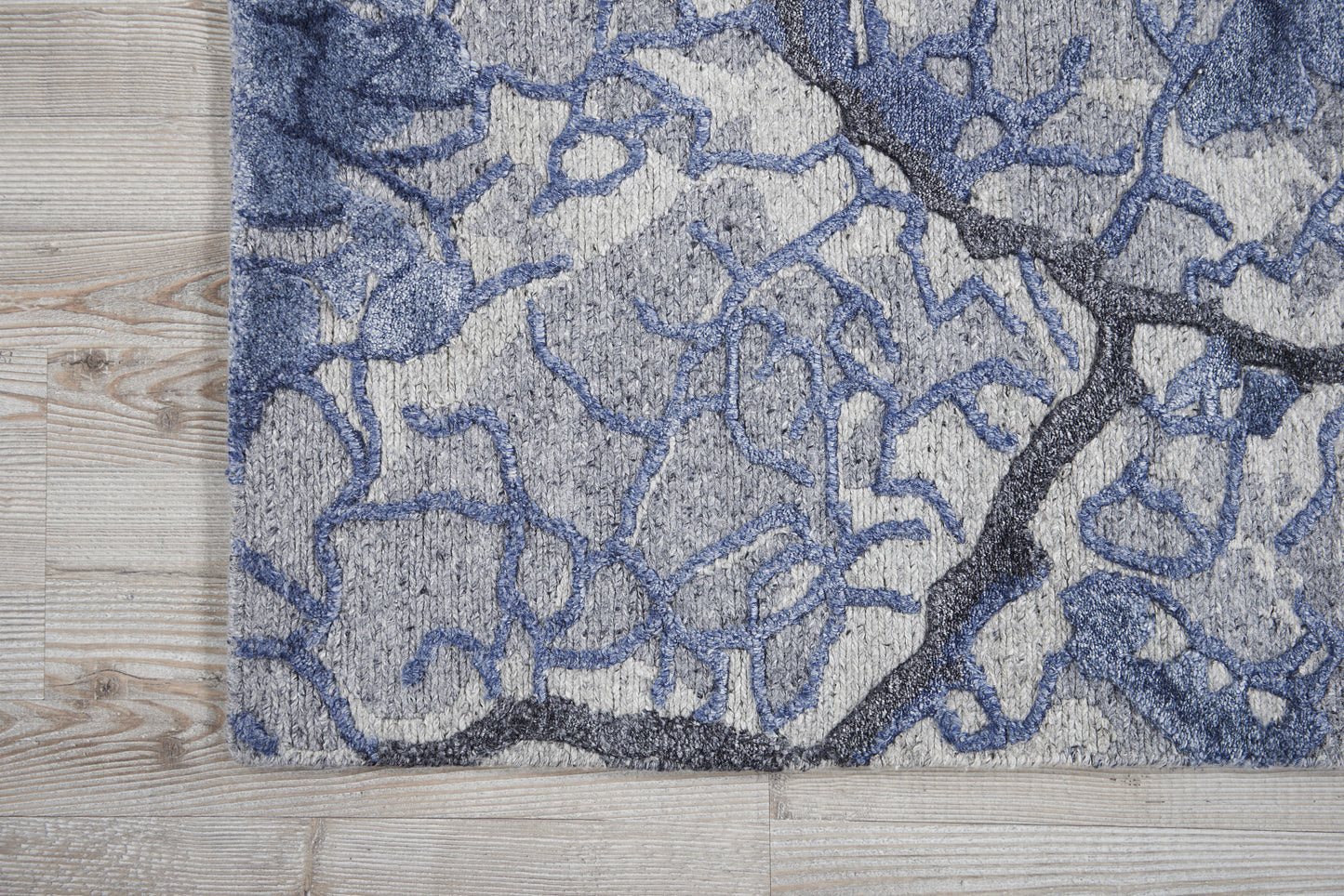 Abstract blue-gray rug with dark navy crack pattern on light gray base; plush tufted pile on wood floor.