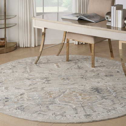 Round neutral-toned patterned area rug in gray-beige under a cream desk and light wood chair in a bright home office.