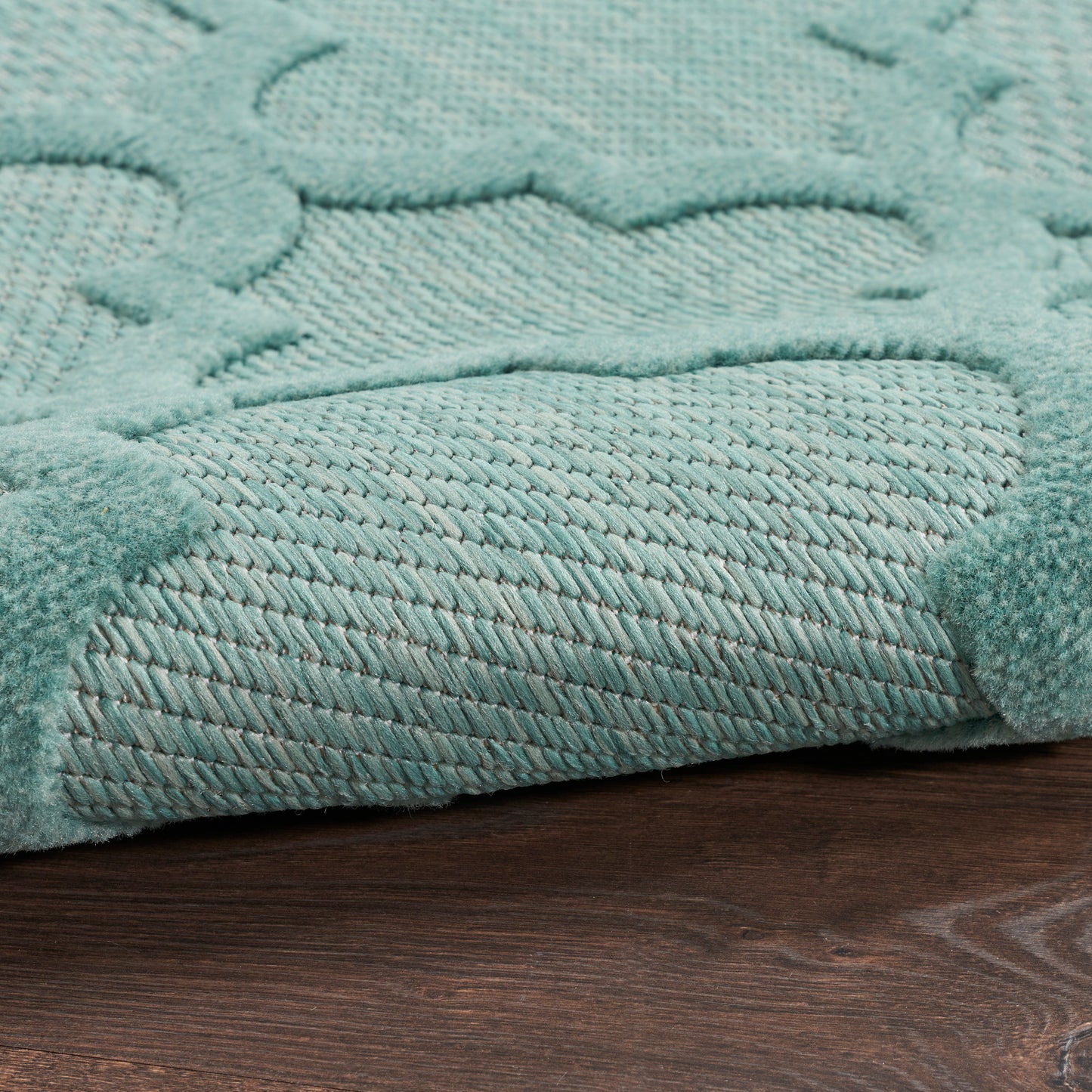 Teal textured outdoor runner rug with a raised pattern and plush pile, folded corner on dark wood floor.