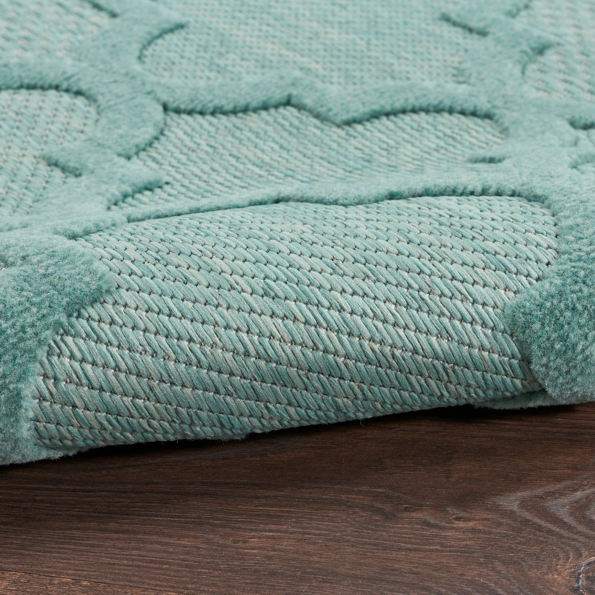 Teal textured outdoor runner rug with a raised pattern and plush pile, folded corner on dark wood floor.