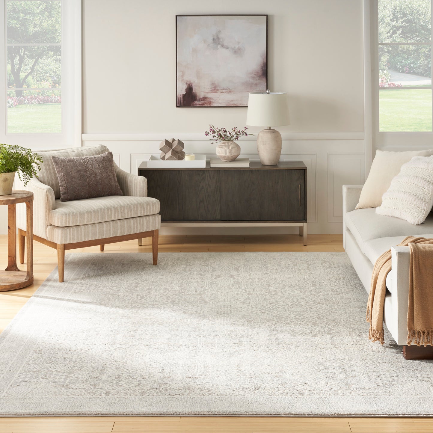 Bright living room with beige walls, neutral sofa & chair, dark wood sideboard, and a soft pink-gray abstract rug (6' x 9').