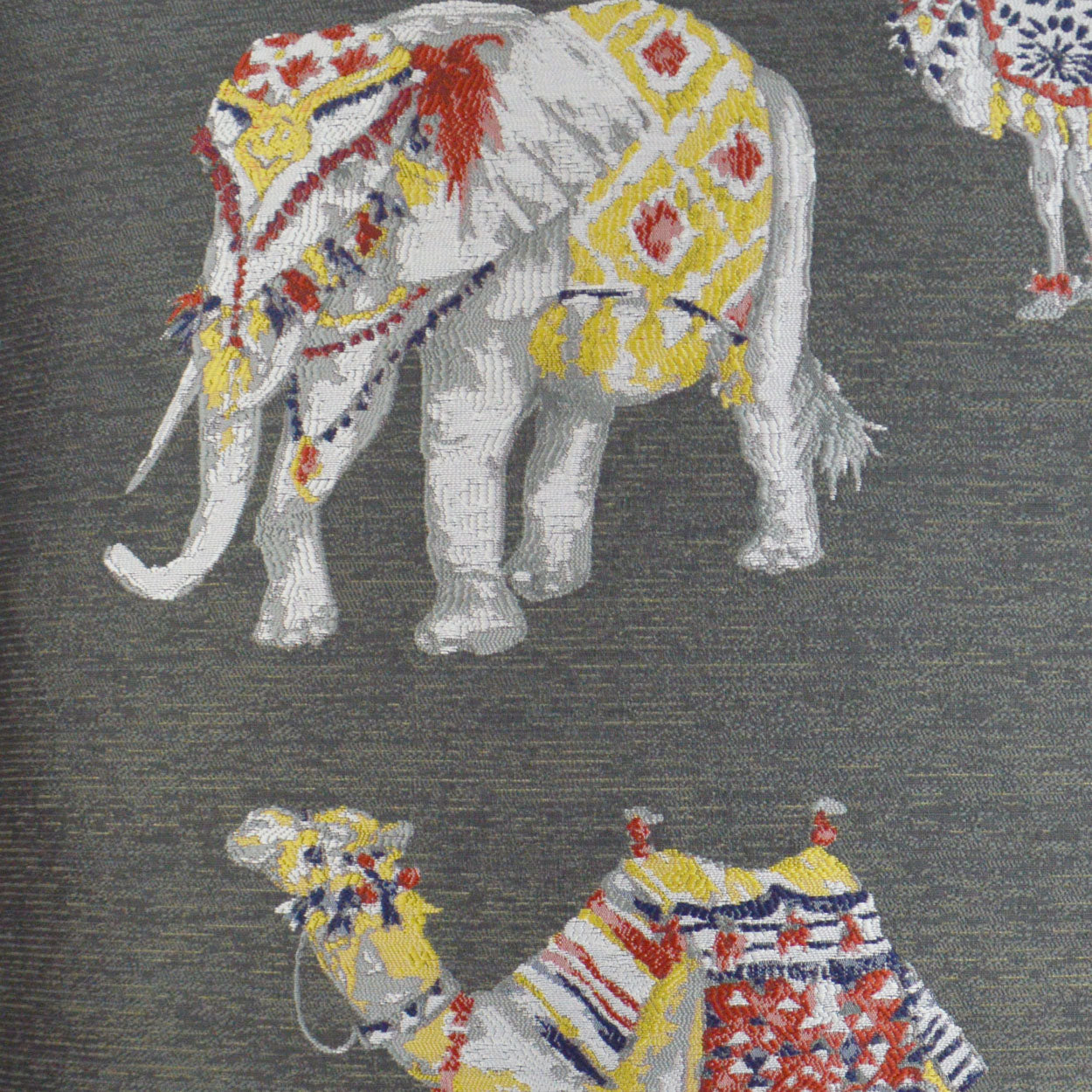 Embroidered fabric with colorful, decorated elephants and tassels on a dark grey background.
