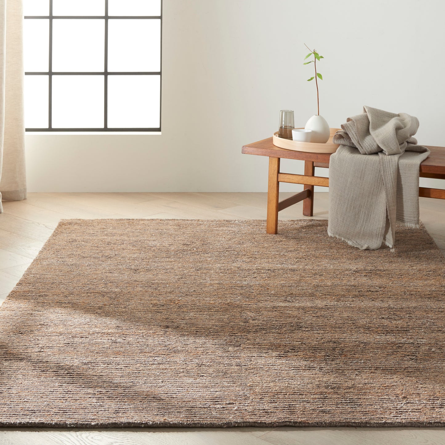 Natural brown textured jute rug in a cozy living space with beige throw on a wooden bench and a potted plant.