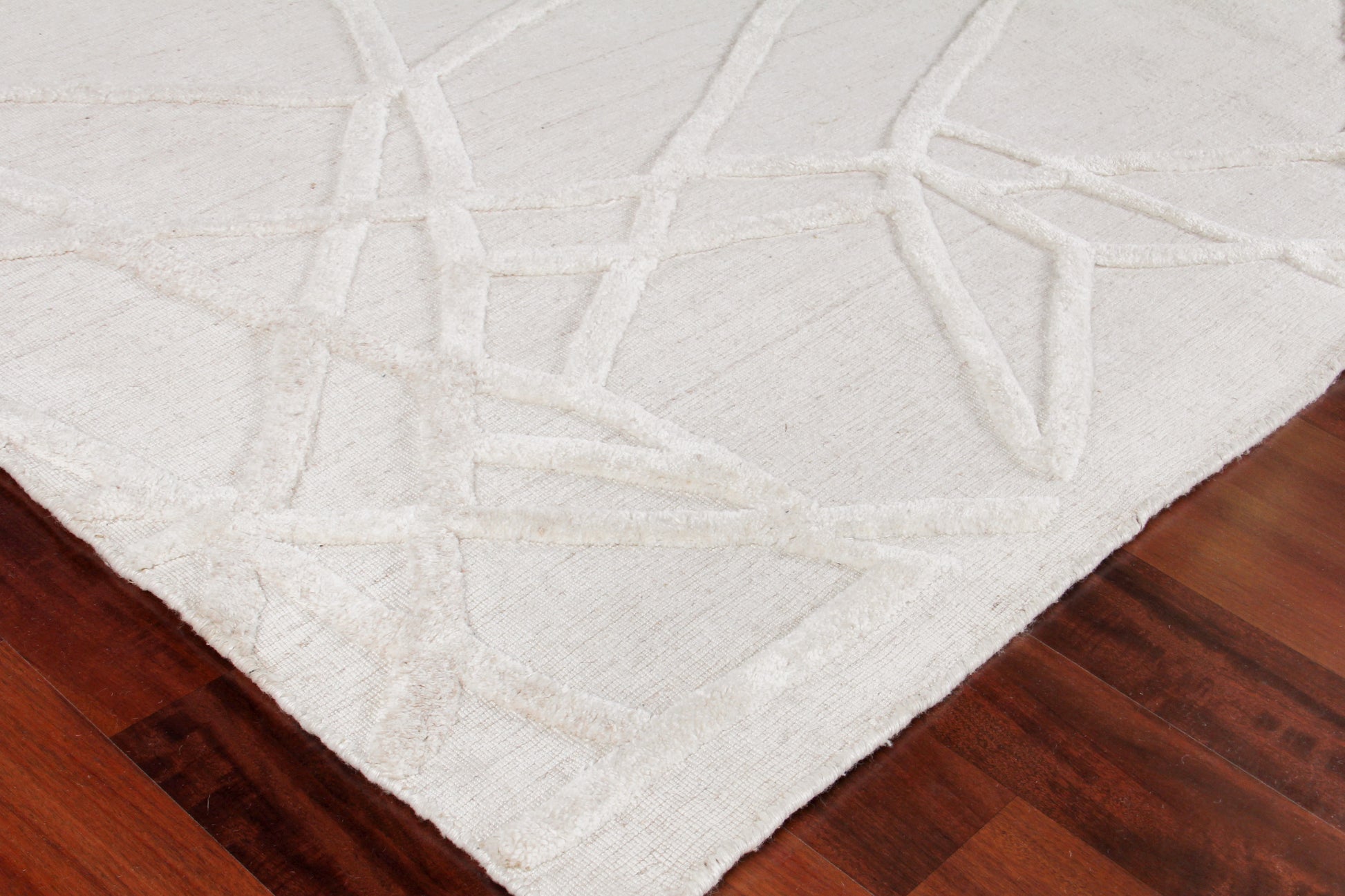 White hand loomed area rug with abstract intersecting loop pattern on dark wood floor.