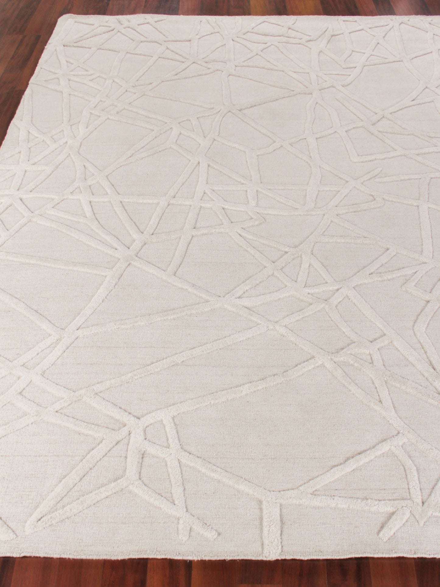 Cream ivory area rug with abstract geometric intersecting line pattern on wooden floor.