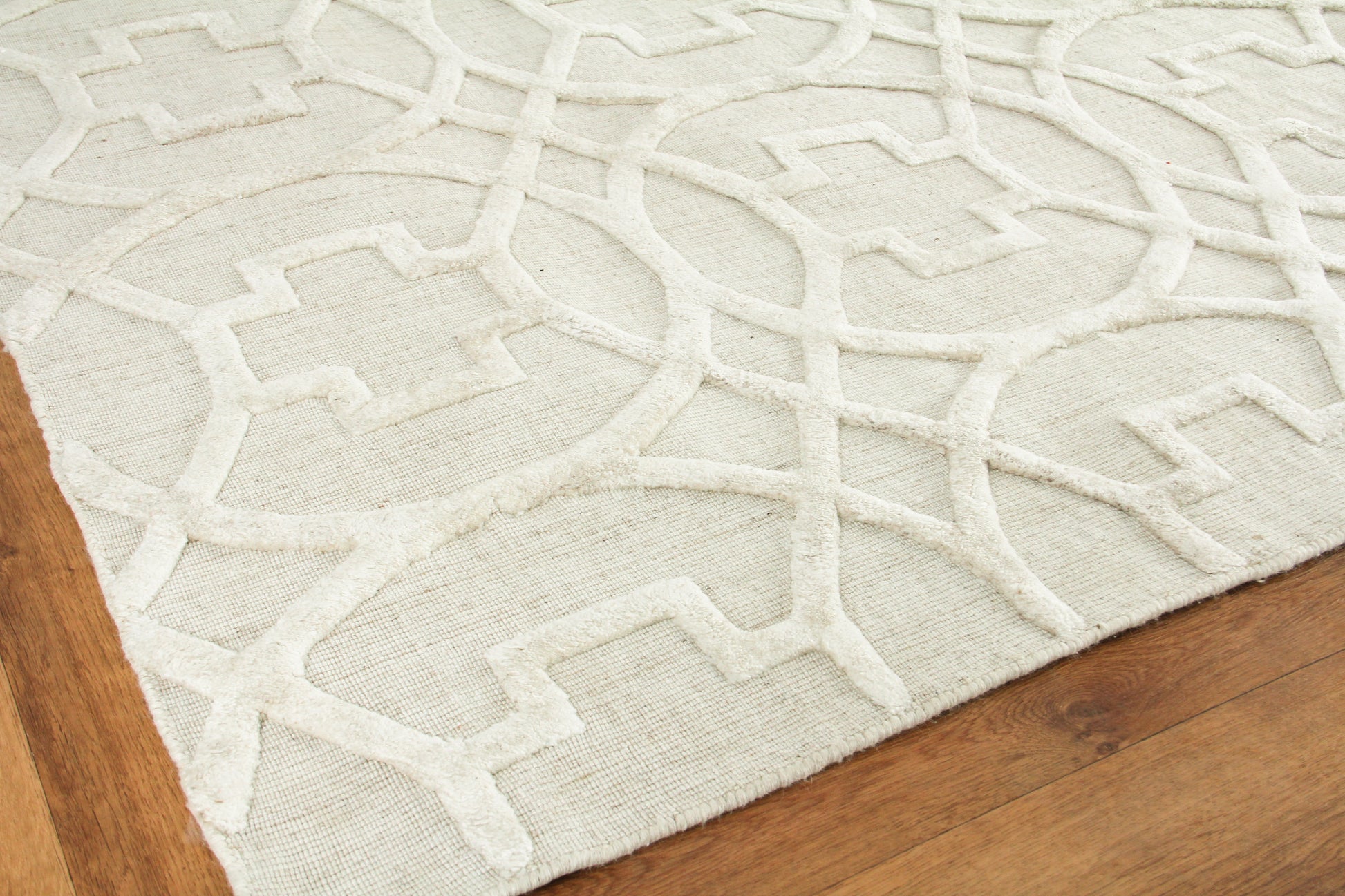 Cream rug with raised white geometric lattice pattern on beige base, bound edges, on wooden floor.