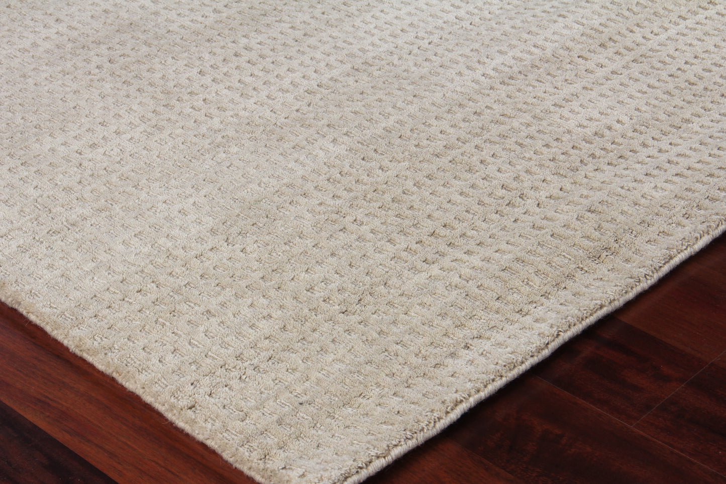 Beige rectangular rug with textured woven loop pattern on dark hardwood floor.