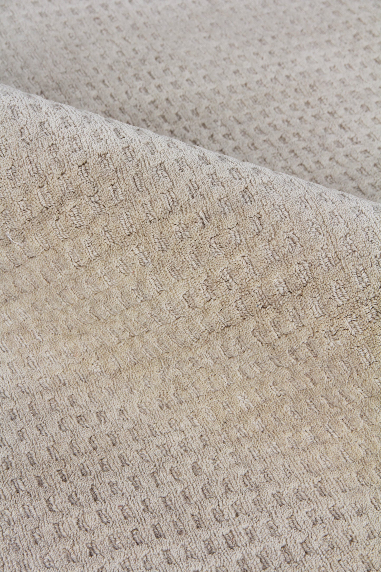 Beige close-up of a waffle-knit New Zealand wool rug with soft folds; textured, neutral rug.