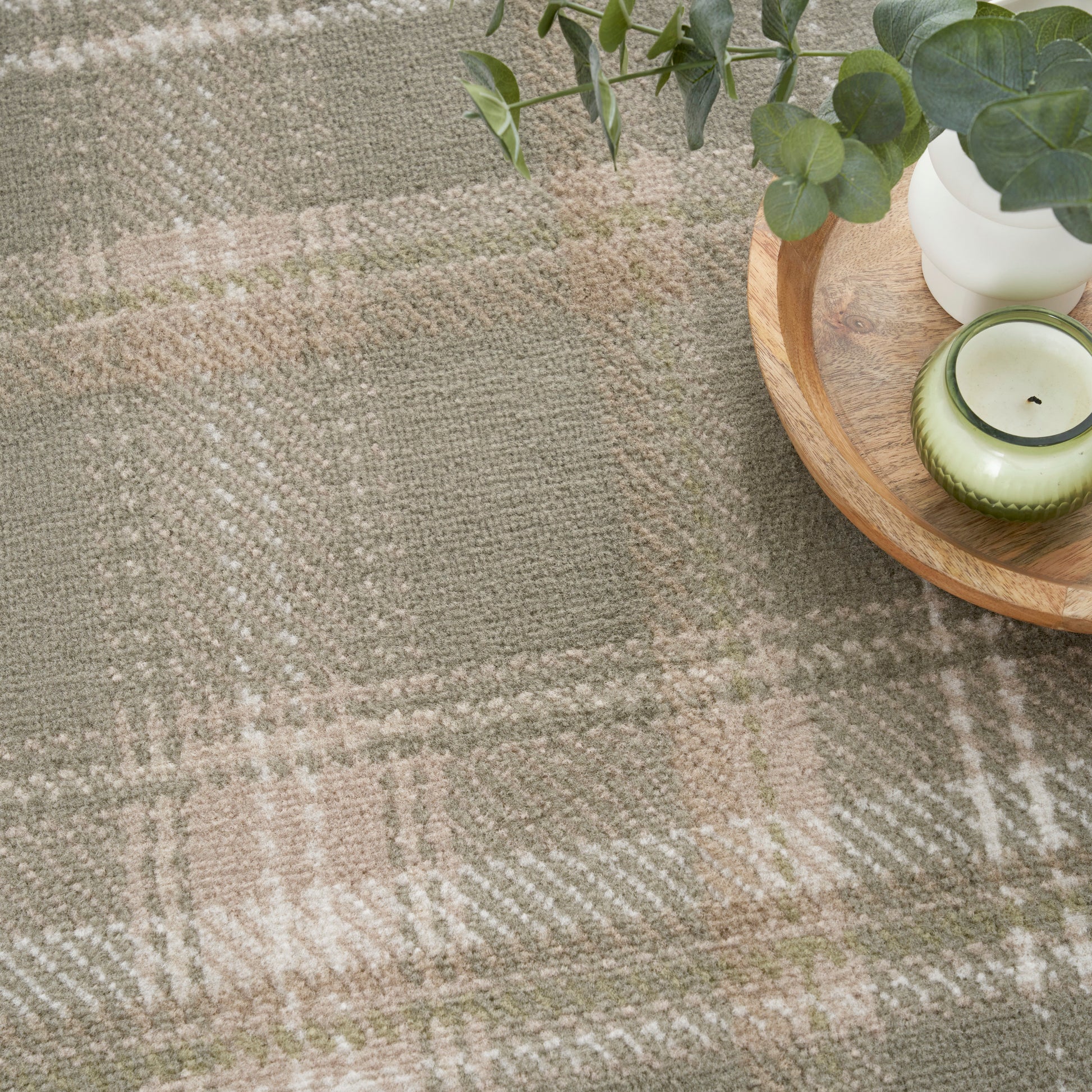 Sage green plaid rug with soft texture; round wooden tray holds a white pot with eucalyptus leaves and a green candle.
