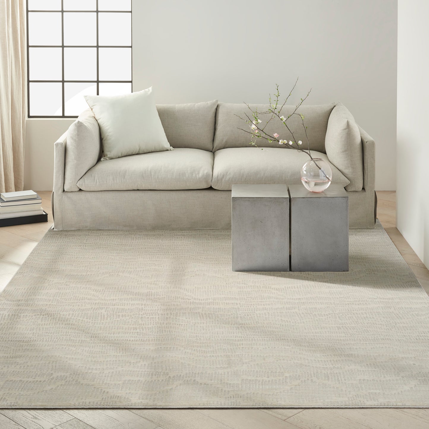 Beige fabric sofa with pale cushions in a bright minimalist living room; concrete block side tables with glass vase.
