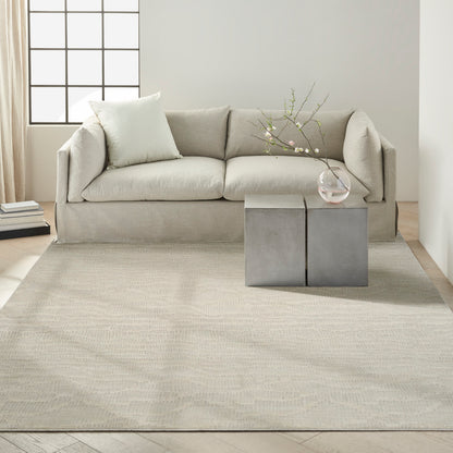 Beige fabric sofa with pale cushions in a bright minimalist living room; concrete block side tables with glass vase.