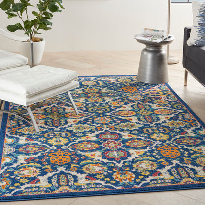 Colorful oriental rug with blue, orange and yellow floral motifs on a light wood floor beside a white lounge chair.