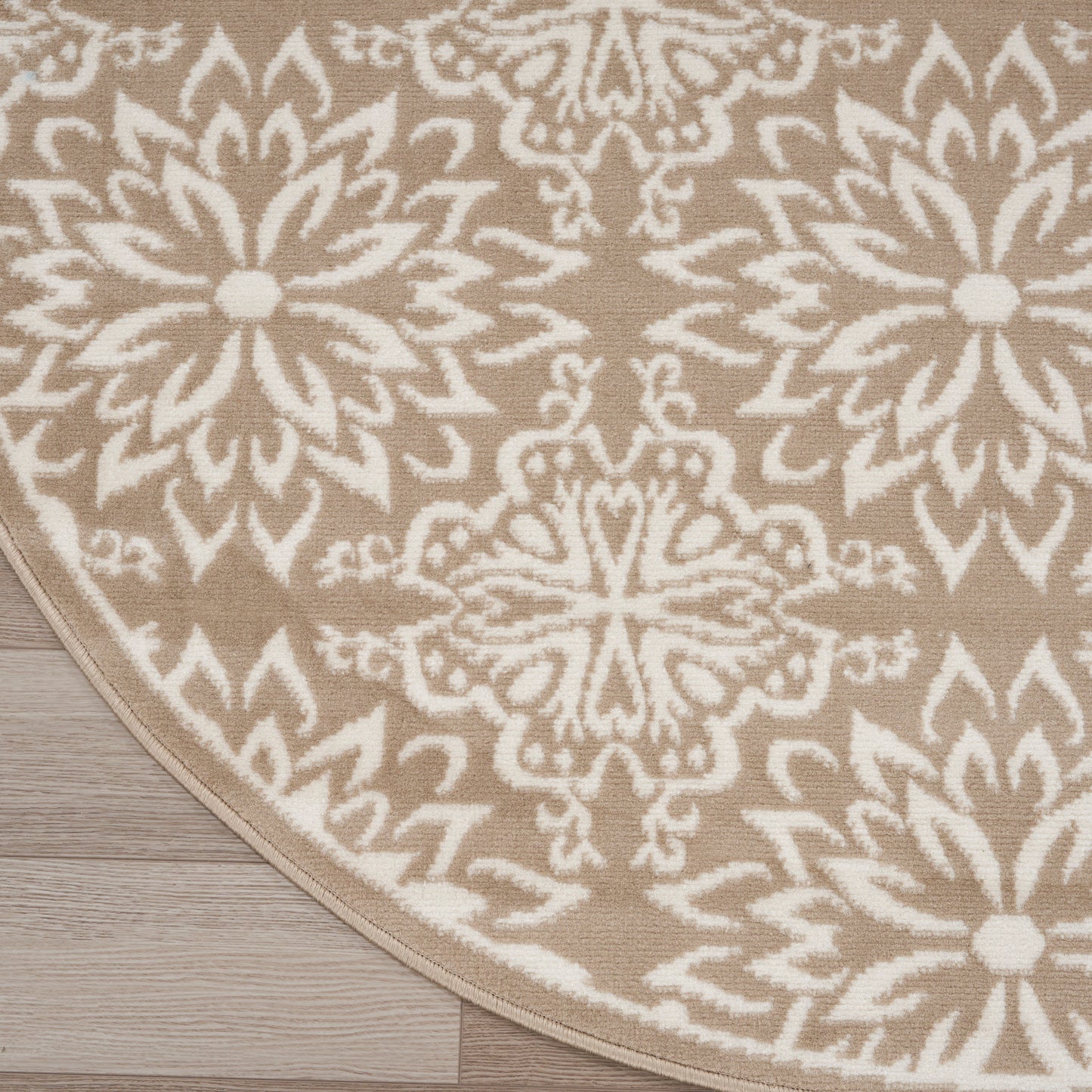 Round beige rug with white geometric floral medallion pattern on light wood floor.