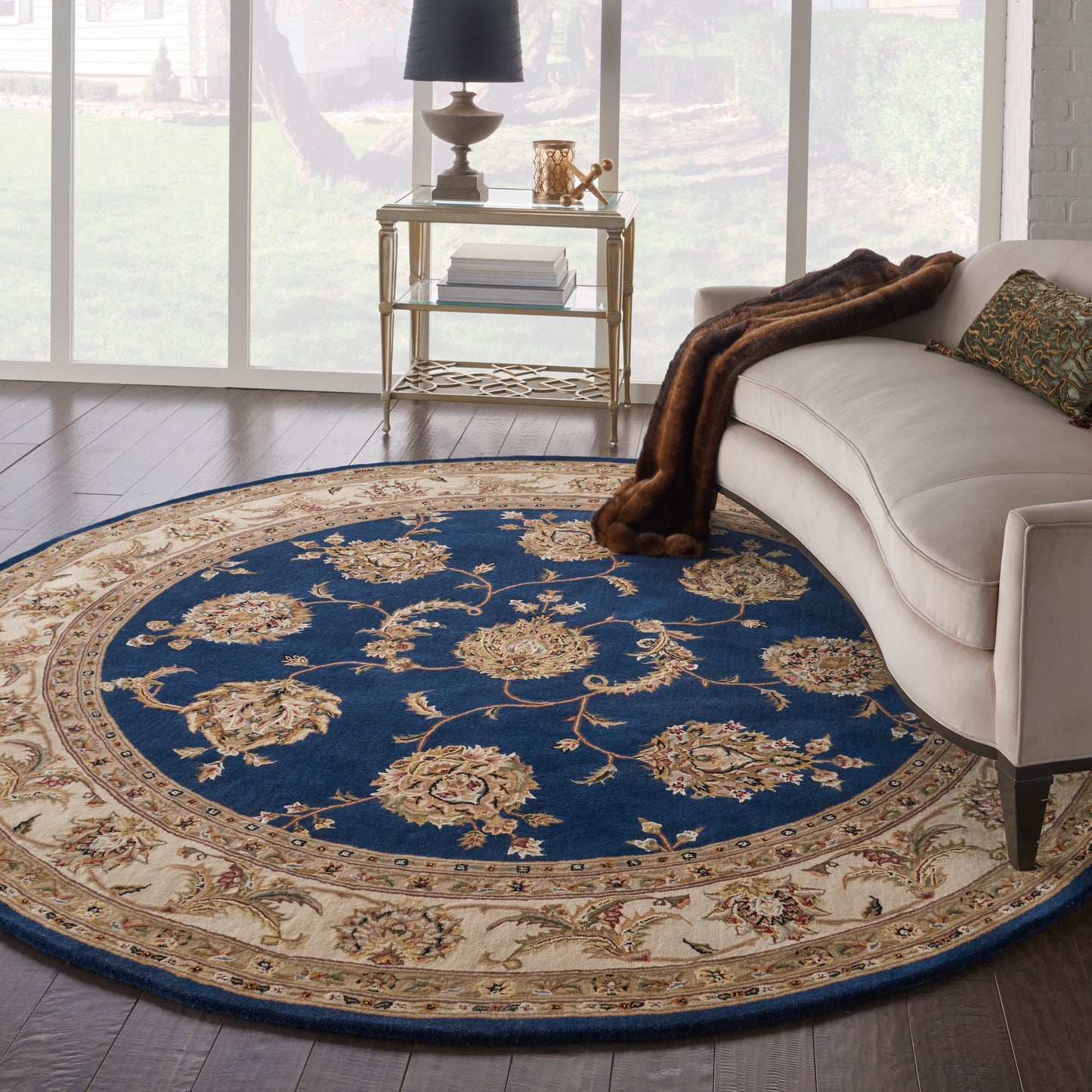 Round oriental rug with navy blue center & beige floral border; beige sofa, faux fur throw, gold metal side table.