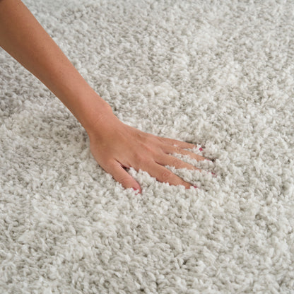 Cream shag rug with long plush pile; hand presses into soft, fluffy fibers.