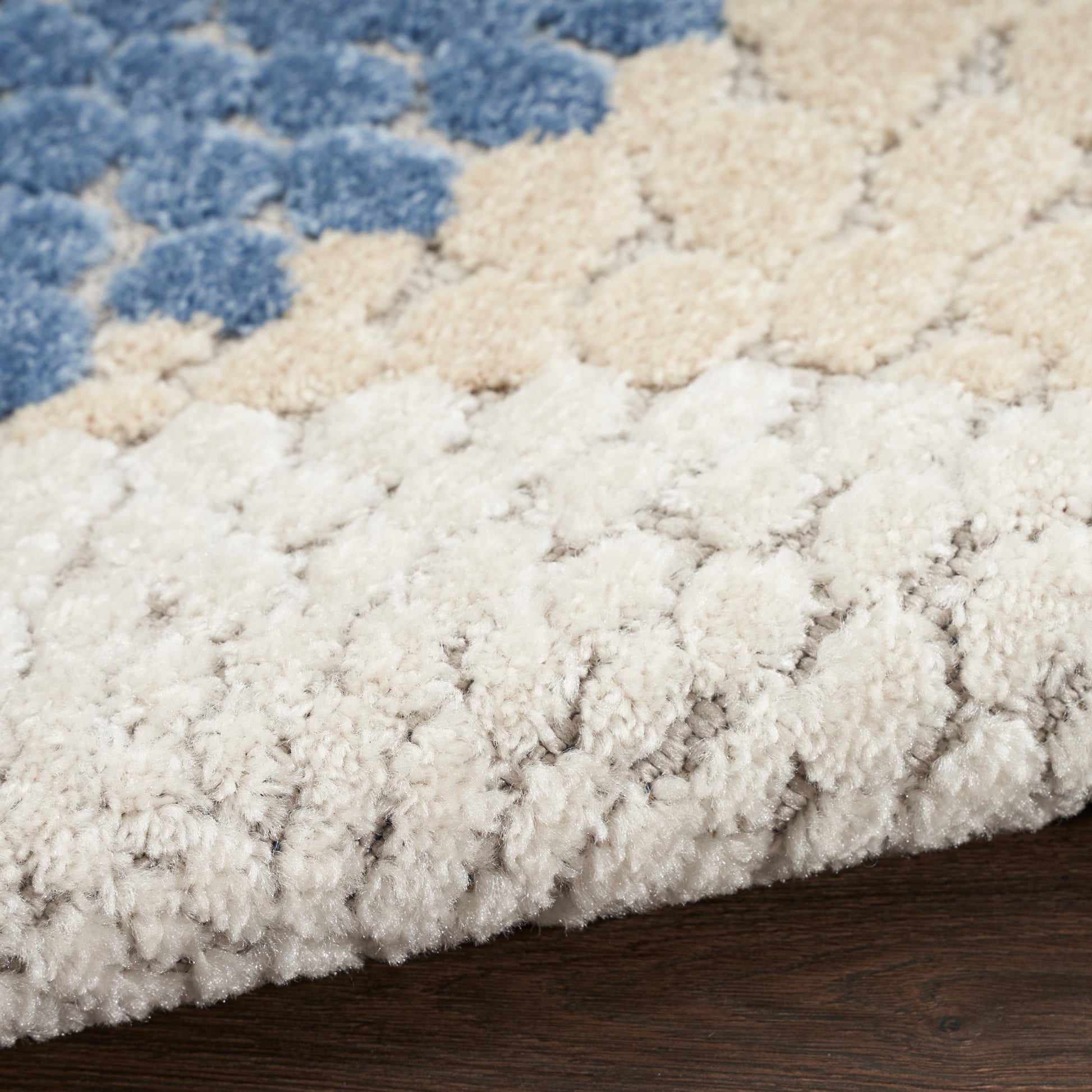 Close-up of a plush shaggy rug with blue, beige and cream tufted circles on a dark wood floor.